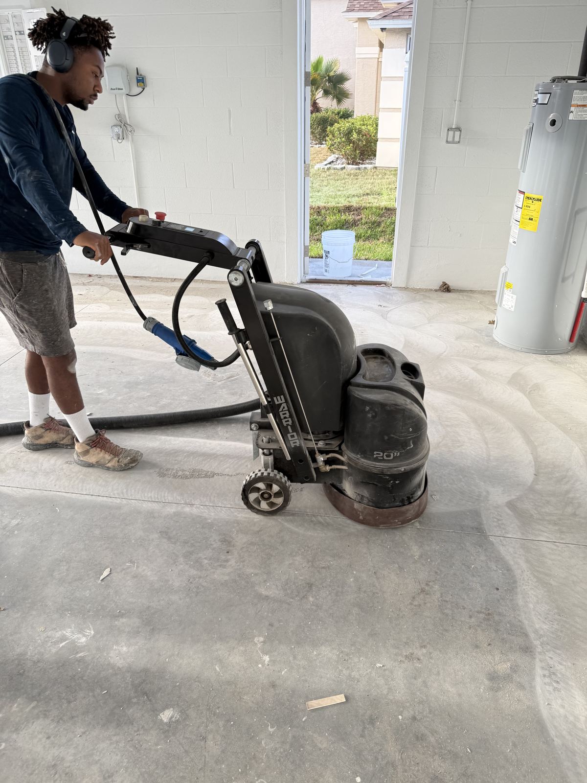 Crew diamond grinding a garage slab with dust extraction before coating
